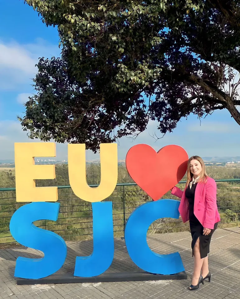 Vanessa Fortes ao lado do letreiro Eu amo SJC em área aberta